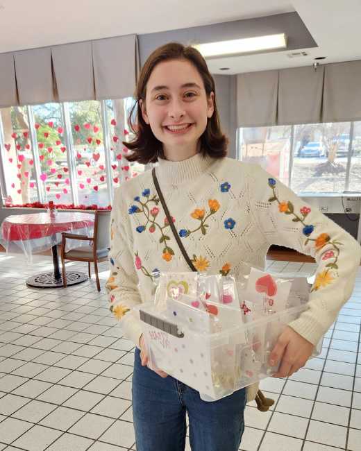 A volunteer holding a basket full of handmade cards in a community space decorated with paper hearts